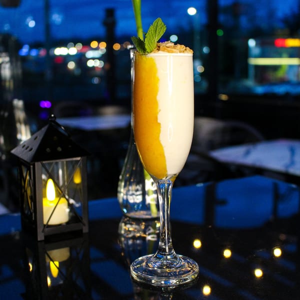 A layered mango and cream drink with mint and granola, next to a lantern at night.