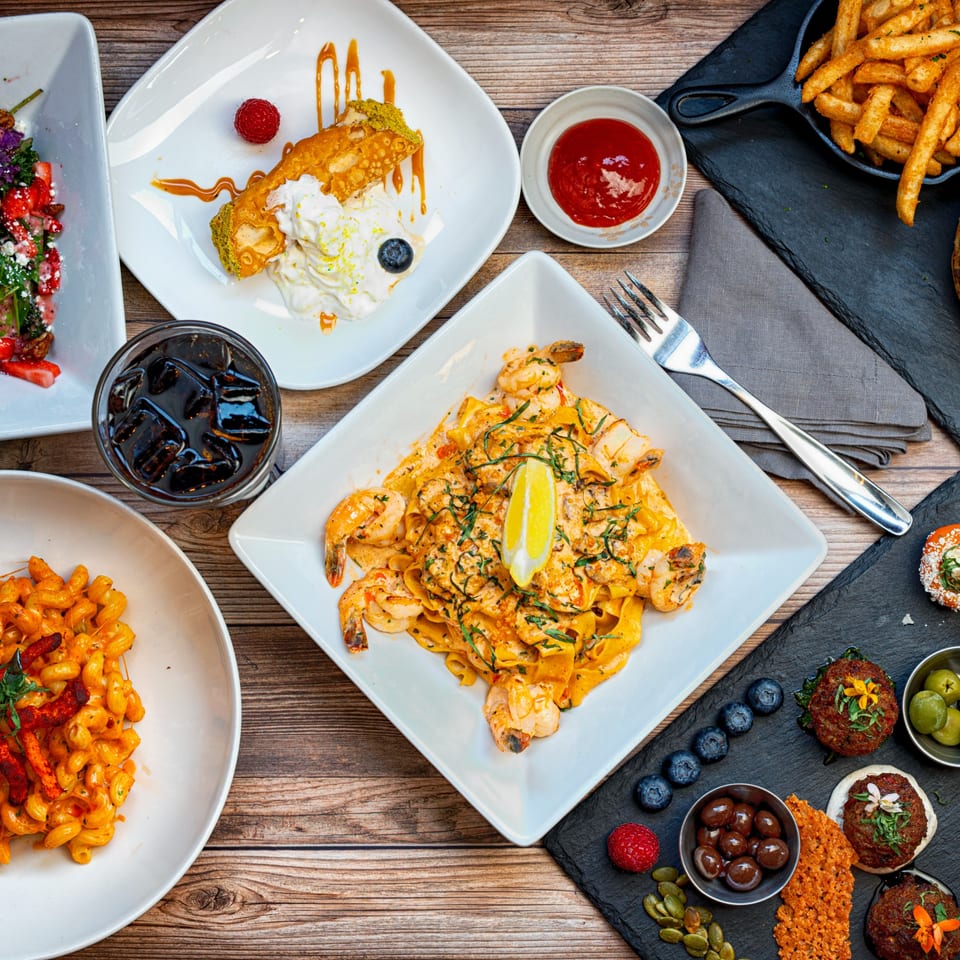 An overhead shot of a wooden table laden with various dishes, including pasta, fries, and desserts.