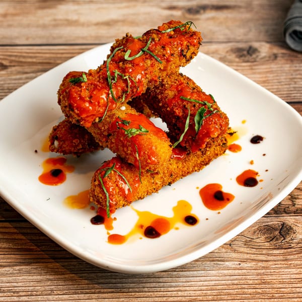 Crispy fried mozzarella sticks drizzled with red sauce and green herbs on a white plate.