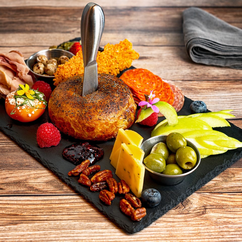 Charcuterie board with baked brie, meats, cheeses, olives, fruit, and nuts on a wooden table.