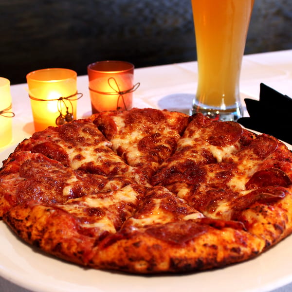 A Sliced pepperoni pizza with melted cheese, candles, and a beer on a white tablecloth.
